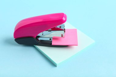 Mavi arka planda yapışkan notları olan pembe zımba.