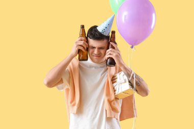 Akşamdan kalma ve sarı arka planda doğum günü partisinden sonra bira içen genç adam.