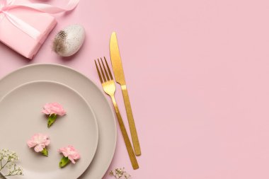 Şirin Paskalya sofrası, pembe arka planda hediyeler, çiçekler ve yumurtalar.