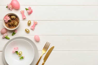 Beyaz ahşap arka planda çiçekler ve yumurtalarla süslenmiş modern Paskalya sofrası.