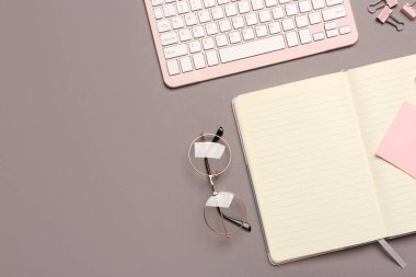 Gri arka planda not defteri, klavye ve gözlüklü kompozisyon. Üst görünüm