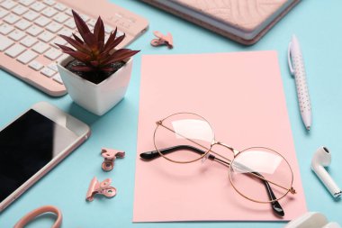 Mavi zemin üzerinde pembe kağıt, gözlük ve kaktüs olan kompozisyon