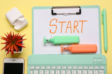 Metin START 'lı pano, işaretleyiciler ve klavye sarı arka planda. Yakın çekim.