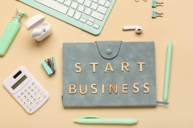 Bej arka planda Start BUSINESS, hesap makinesi ve kulaklığı olan bir defter. Üst görünüm