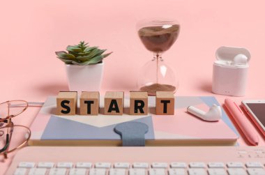 Pembe zemin üzerinde START, not defteri ve kum saati olan küp