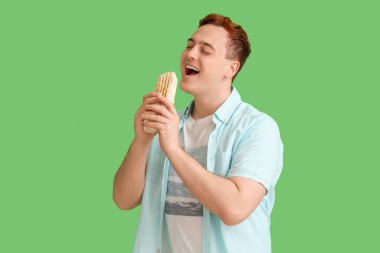 Genç mutlu adam yeşil arka planda donör kebabı yiyor.