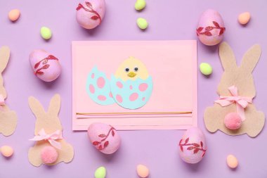 Paskalya tavşanları, boyalı yumurtalar ve eflatun kaplama tavuklu kartlar. Üst görünüm