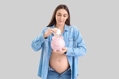 Genç hamile bir kadın arka planda kumbaraya para yatırıyor. Annelik Faydası kavramı