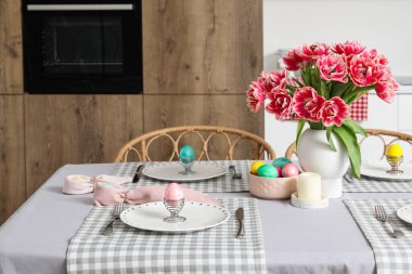 Mutfaktaki yemek masasında vazo lale, paskalya yumurtası ve yemek takımı.