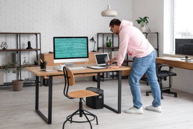 Modern ofiste laptop ve bilgisayarla çalışan erkek programcının portresi