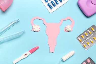 Mavi arka planda jinekolojik spekulumlu kağıt rahim, haplar, tampon ve hamilelik testi.