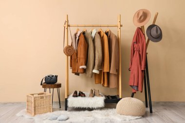 Bej duvarın yanında şık kıyafetler ve elbise askısı var.