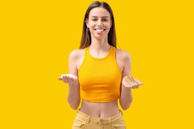 Doğum kontrol hapları ve sarı arka planda vajinal fitilleri olan güzel bir genç kadın.