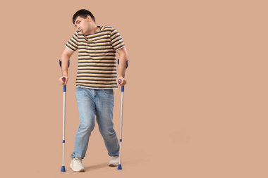 Kahverengi arka planda koltuk değnekleri olan genç bir adam. Ulusal Beyin Felci Farkındalığı Ayı