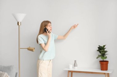 Duvarında küf olan genç bir kadın evde cep telefonuyla konuşuyor.