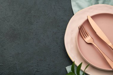 Siyah arkaplanda pembe tabaklar ve çatal bıçak takımı, yakın plan.