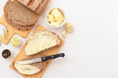 Tahta tahtalar taze tereyağlı, sarımsaklı ve biberli ekmek dilimleri beyaz arka planda.