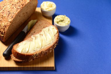 Tahta tahta tahta, ekmek dilimleri ve mavi arka planda taze tereyağı.