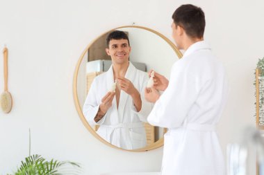 Banyoda aynanın yanında serumu olan genç bir adam.