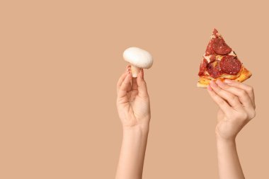 Bej arka planda pizza dilimi ve mantar tutan kadın eller.