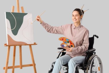 Tekerlekli sandalyedeki kadın ressam boya paleti ve hafif arka planda sehpası var.