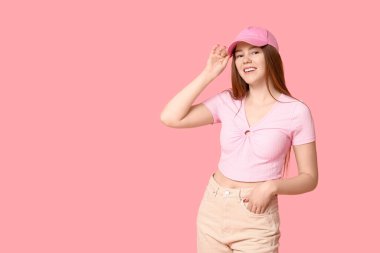 Beyzbol şapkalı şık bir genç kız, pembe arka planda üstü ve pantolonu.