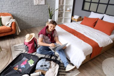 Otel odasında bavulları açarken dizüstü bilgisayar kullanan erkek turist