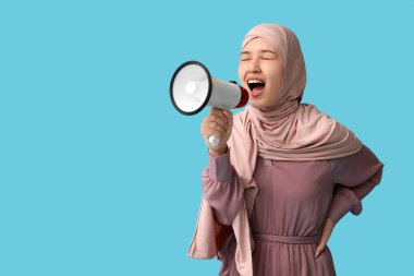 Genç Asyalı Müslüman kadın mavi arka planda megafona bağırıyor. Ulusal Duyulma Günü