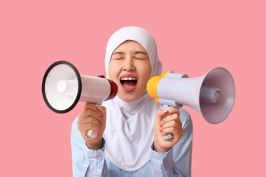 Genç Asyalı Müslüman kadın pembe arka planda megafonlara bağırıyor. Ulusal Duyulma Günü