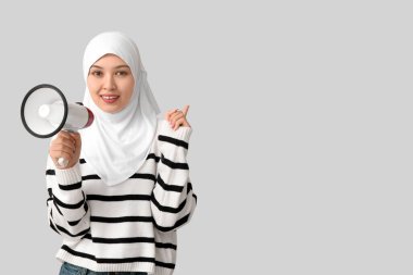 Megafonlu genç Asyalı Müslüman kadın gri arka plandaki bir şeyi işaret ediyor. Ulusal Duyulma Günü