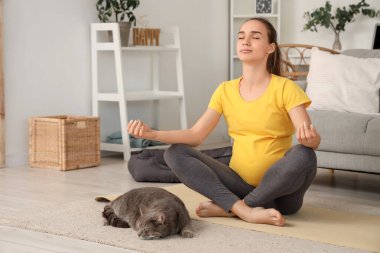 Evde meditasyon yapan genç hamile bir kadın.