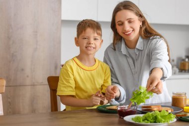 Sevimli küçük çocuk ve annesi mutfakta salatayla tost yapıyorlar.