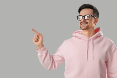 Gözlüklü genç adam gri arka planda bir şeye bakıyor.