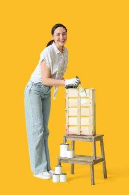 Sarı arka planda tahta kutu boyayan genç bir kadın.