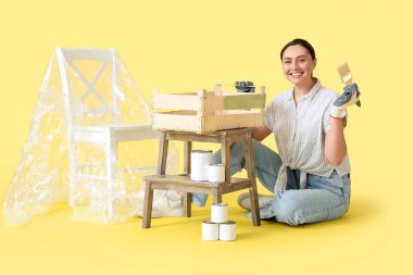 Sarı arka planda tahta kutu boyayan genç bir kadın.