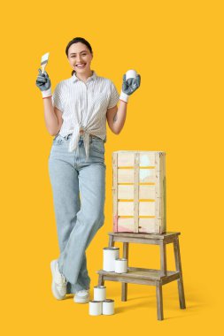 Fırçalı ve sarı arka plana tahta kutu çizebilen genç bir kadın.