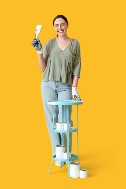 Sarı arka planda resim yapan genç bir kadın.