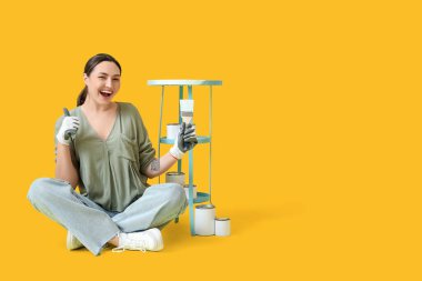 Sarı arka planda fırça ve teneke kutuları olan genç bir kadın.