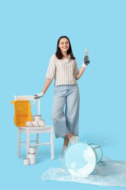 Fırça ve teneke kutularla masayı mavi arka plana boyayan genç bir kadın.