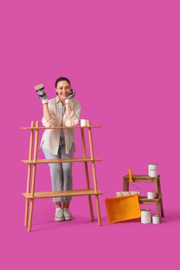 Mor arka planda ahşap raf ünitesi boyayan genç bir kadın.