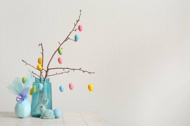 Mavi vazoda Paskalya yumurtası, hediye yumurtası ve beyaz arka planda tavşan olan dallar.