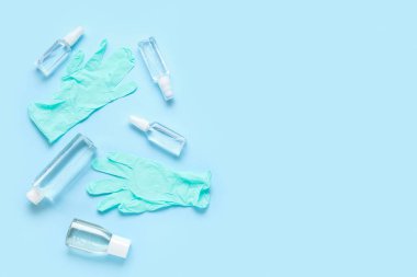 Mavi arka planda farklı şişe dezenfektanları olan lastik eldivenler.