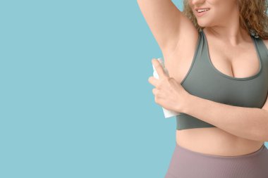 Genç bir kadın mavi arka plana deodorant sürüyor, yakın plan.