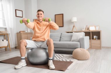 Sportif bir genç adam evde spor yaparken dambıllar takıyor.