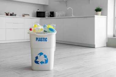 PlaSTIC yazısıyla dolu çöp kutusu ve mutfakta yerde çöp. Geri dönüşüm kavramı
