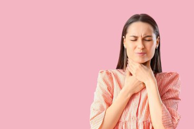 Pembe arka planda boğaz ağrısı çeken genç bir kadın.