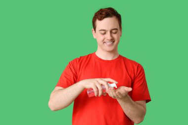 Yeşil arka planda dezenfektan kullanan genç adam.