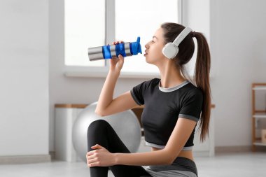 Kulaklıklı, evinde bir şişe su olan genç ve güzel bir bayan.