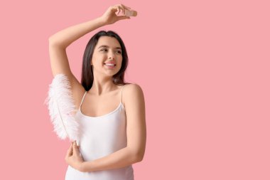 Mutlu gülümseyen genç kadın, pembe arka planda kristal deodorant ve tüyle