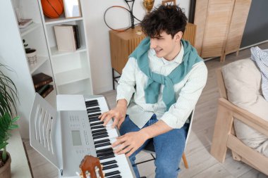 Erkek öğrenci evde sentezleyici oynuyor.